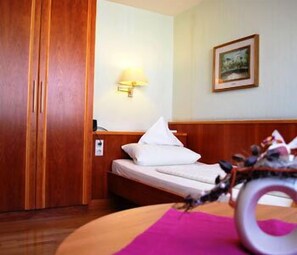 A hotel room with a bed, a nightstand, a lamp, a wooden wardrobe, and a framed picture on the wall. - Weihenstephaner Stuben (Landshut)