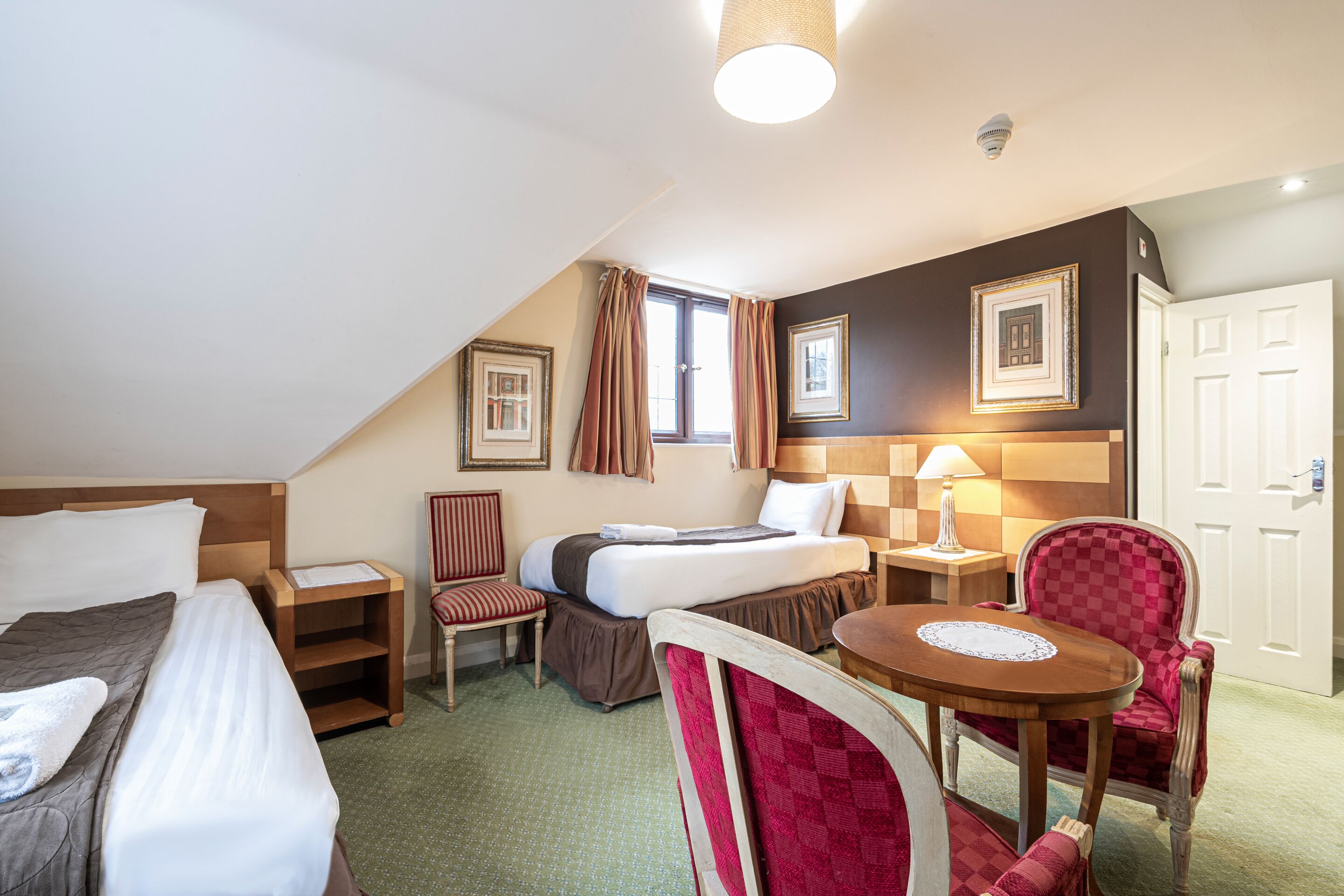 A hotel room with a bed, a desk, a chair, a table, and a lamp.