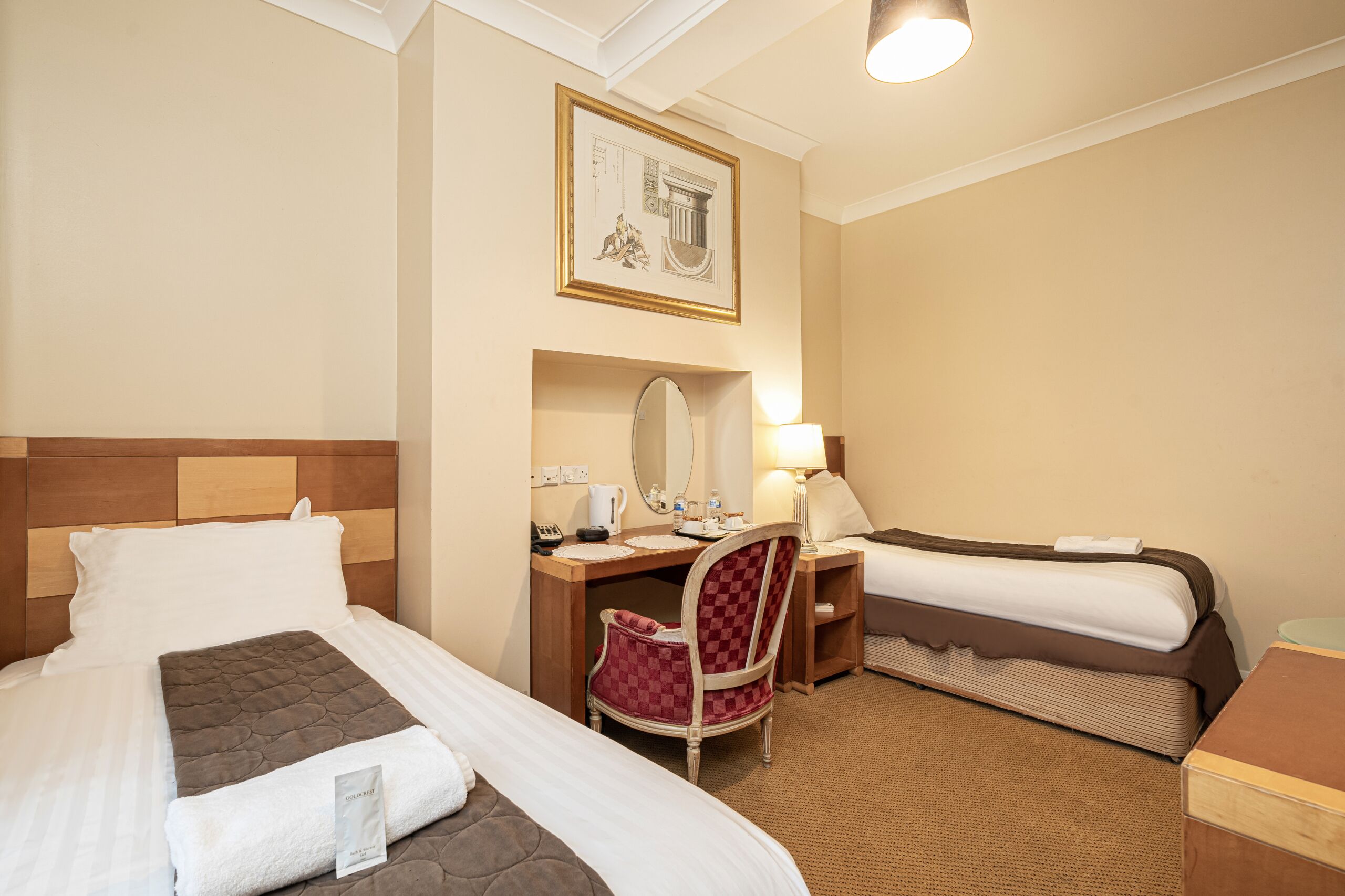 A hotel room with two beds, a desk, a chair, a mirror, and a lamp.