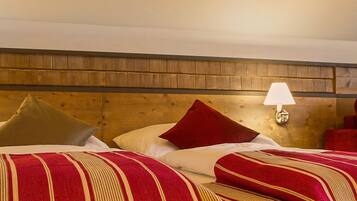 Une chambre d’hôtel avec deux lits, chacun recouvert d’une couverture à rayures rouges et beiges, doté d’une tête de lit en bois et de deux lampes fixées au mur.