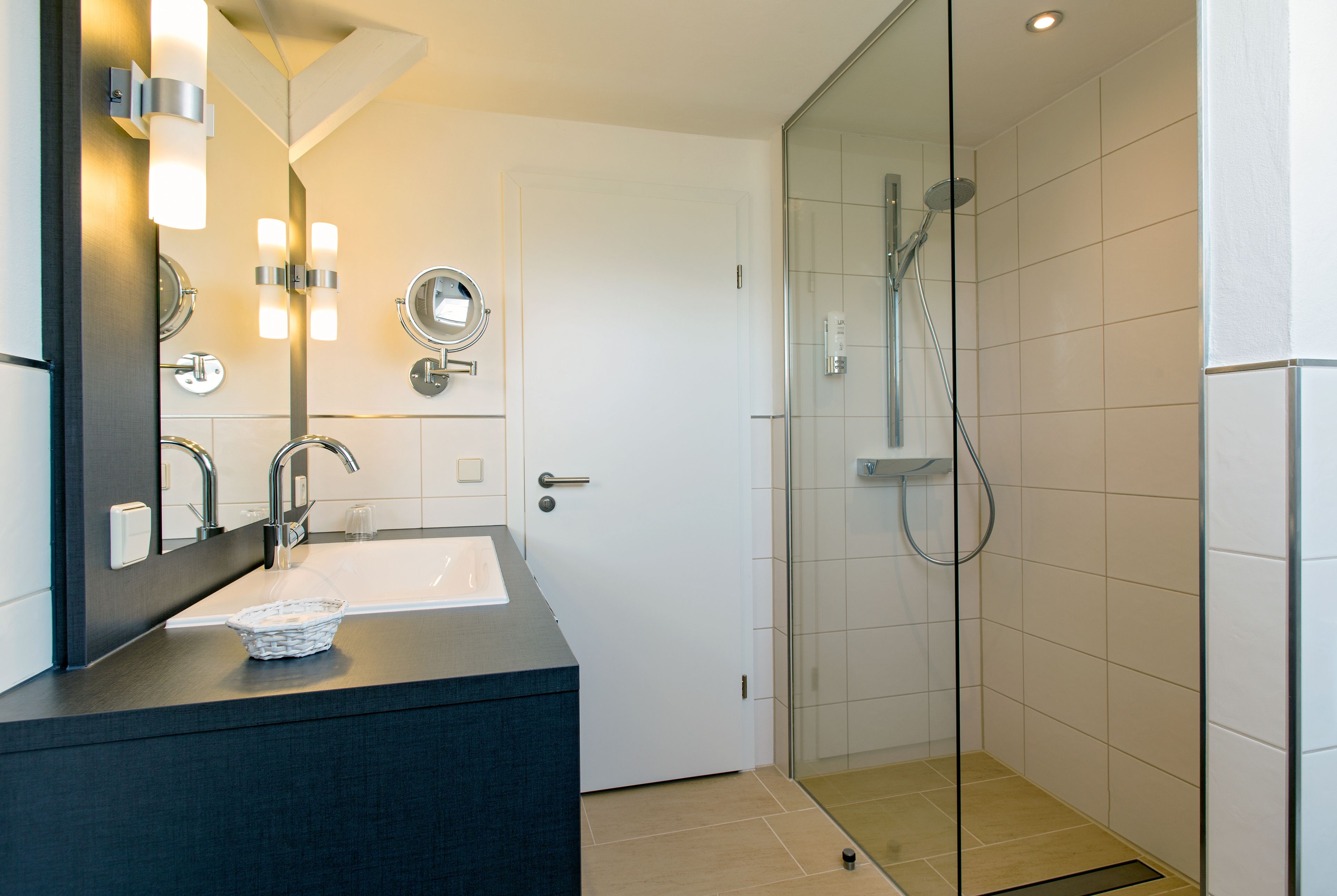 Un baño moderno con ducha envuelta en vidrio, tocador oscuro y lavamanos blanco.