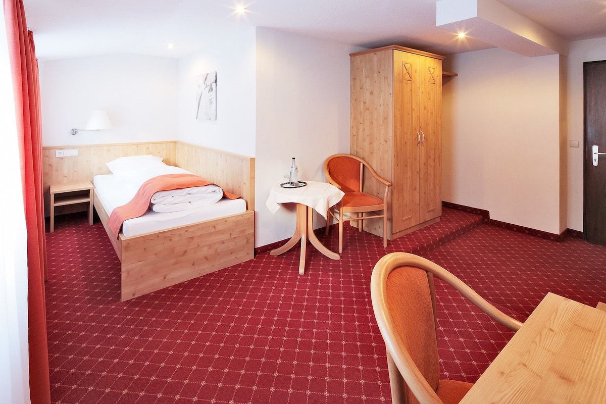 Una habitación de hotel con cama, una silla, una mesita y un armario.