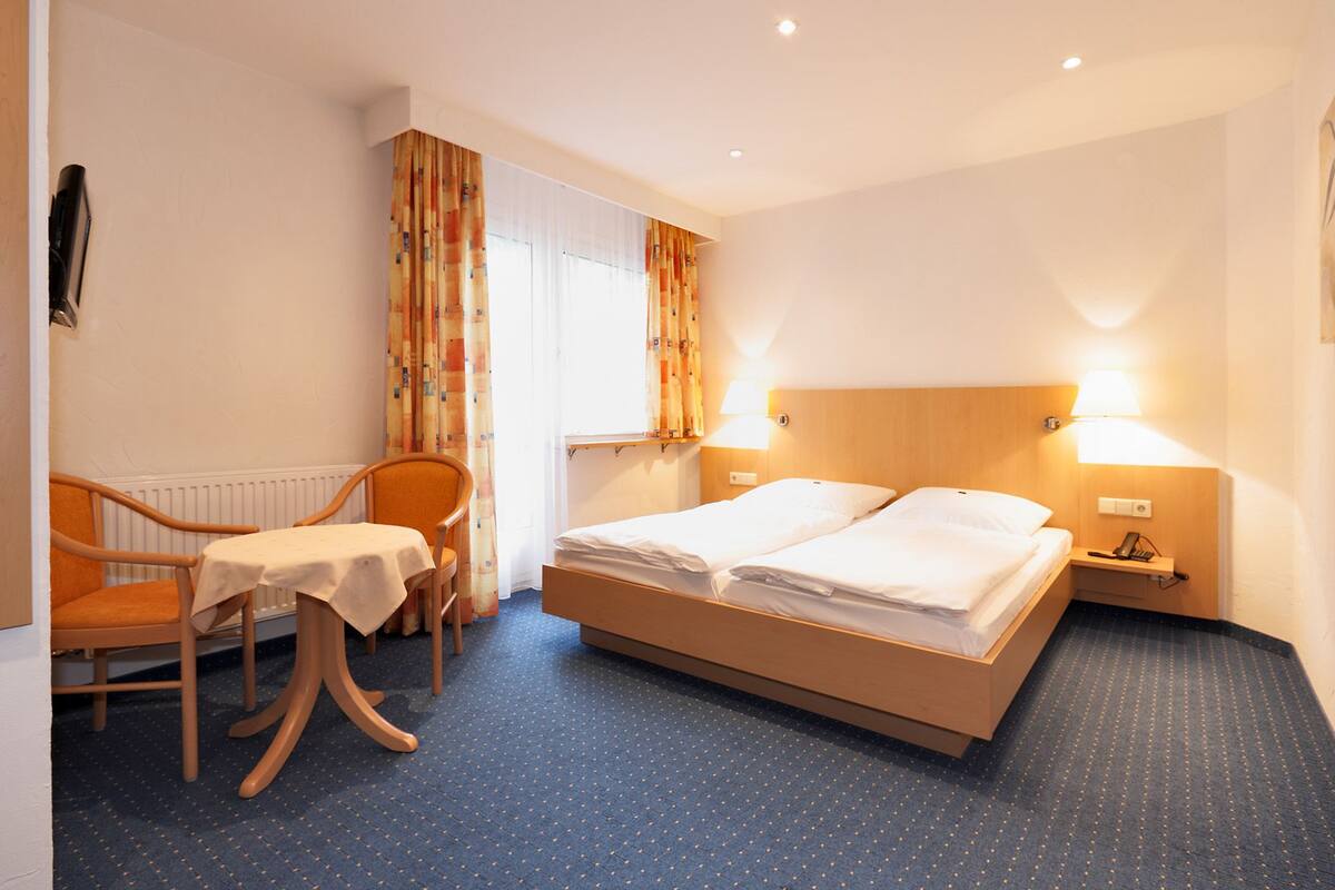 Una habitación de hotel con una cama, una silla, una mesa y un ventanal con cortinas.