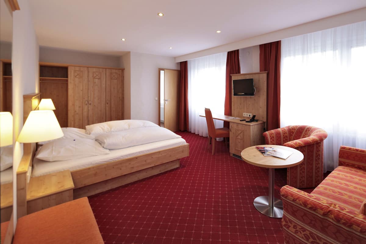 Habitación de hotel con cama, escritorio, silla, televisor y piso cubierto de alfombra roja.
