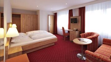 Habitación de hotel con cama, escritorio, silla, televisor y piso cubierto de alfombra roja.