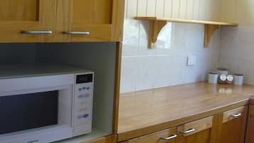 A kitchen with wooden cabinets, a white microwave, and a small shelf with two framed pictures.