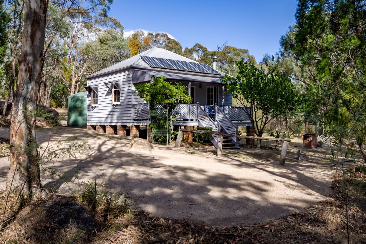 A house with solar panels, surrounded by trees and a dirt path.