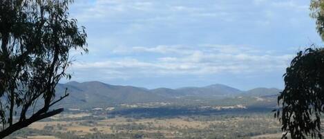A panoramic view of a rural landscape with rolling hills, a small body of water, and scattered trees.