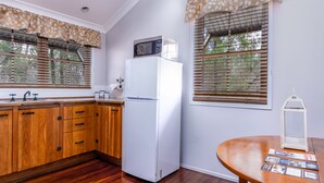 Una cocina con armarios de madera, un refrigerador blanco, un microondas encima, un lavamanos con grifo y una mesa con una linterna.