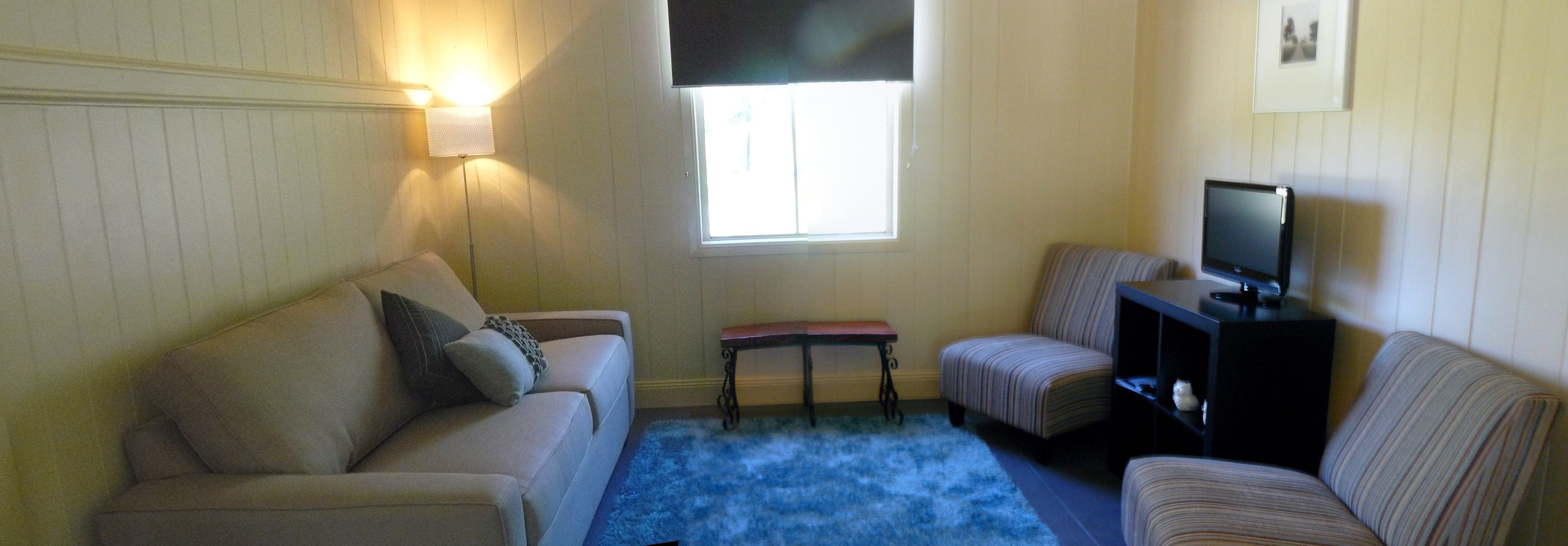 A living room with a beige sofa, a striped armchair, a small table, and a television on a stand.