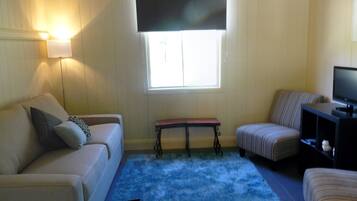 A living room with a beige sofa, a striped armchair, a small table, and a television on a stand.