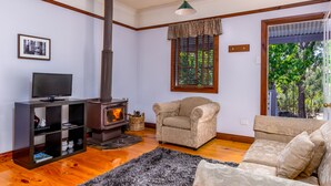 Un salón acogedor con chimenea, un sofá, un televisor sobre un mueble bajo y una ventana con vistas a árboles.