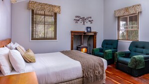 Un dormitorio con una cama, una chimenea y dos sillones verdes.