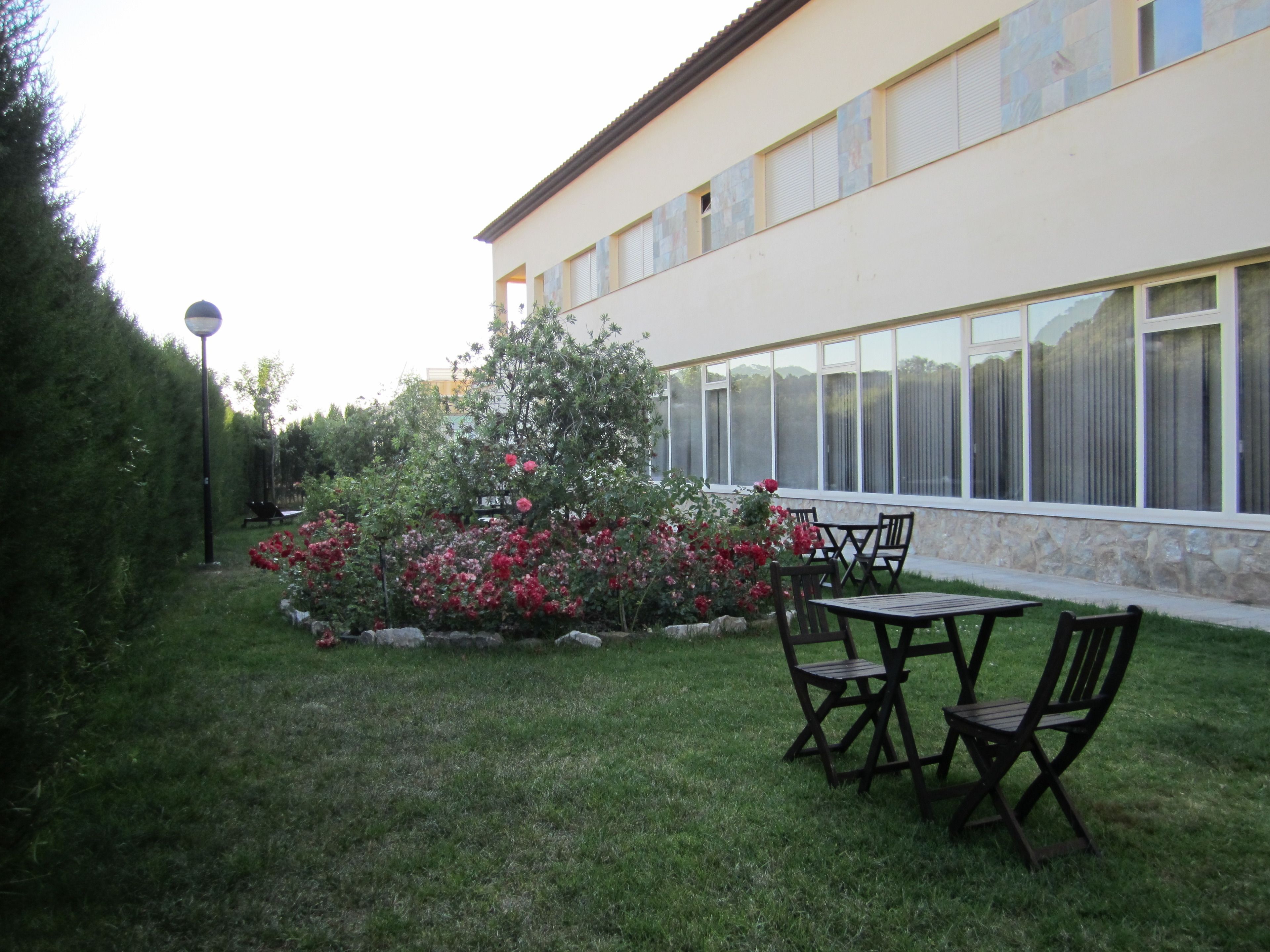 Un edificio con una amplia fachada de ventanales, un césped y un pequeño jardín con flores rojas.