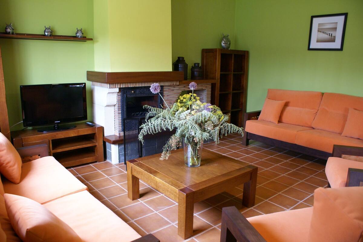 A living room with a wooden coffee table, orange sofa, and a television on a stand.