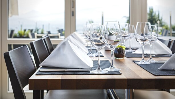 A dining table set with multiple wine glasses, black chairs, and a view of the outdoors. - Hotel Sonnenberg (Kriens)