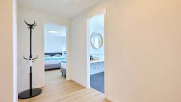 Un pasillo que conduce a un dormitorio con cama, un baño con lavamanos y un perchero.