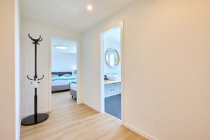 Un pasillo que conduce a un dormitorio con cama, un baño con lavamanos y un perchero.