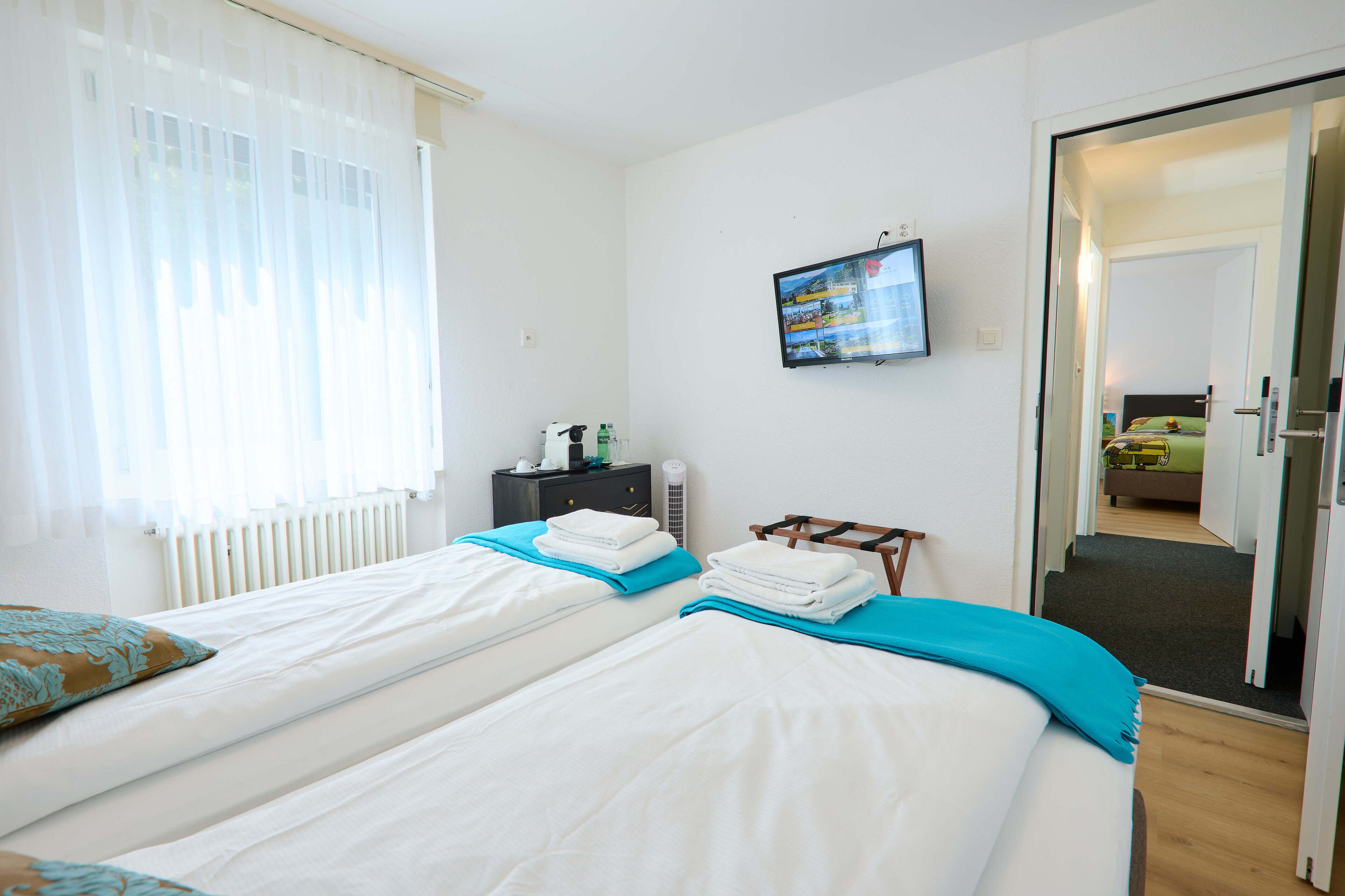 A hotel room with two beds, a TV on the wall, and a door leading to another room.