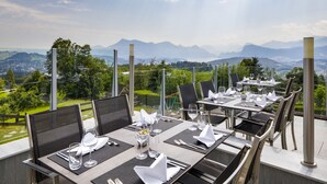 A restaurant with tables set for dining, overlooking a mountainous landscape. - Hotel Sonnenberg (Kriens)