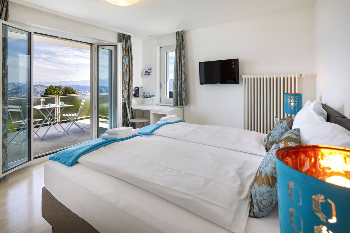 A hotel room with a large bed, a desk, a chair, and a view of the outdoors.