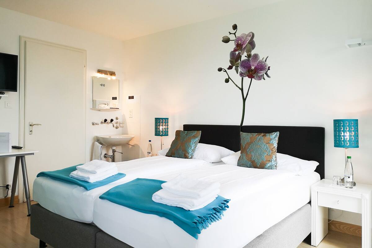 A hotel room with a large bed, a bedside table, a nightstand, a bathroom with a sink and mirror, and a TV on the wall.