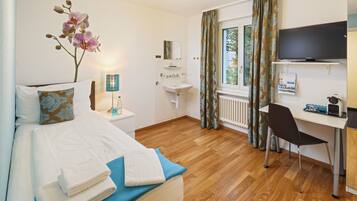A hotel room with a bed, a desk, a chair, a TV, a sink, and a window with curtains.