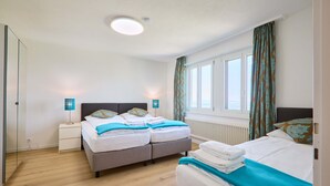 A hotel room with two beds, a nightstand, a lamp, a window with curtains, and a radiator. - Hotel Sonnenberg (Kriens)