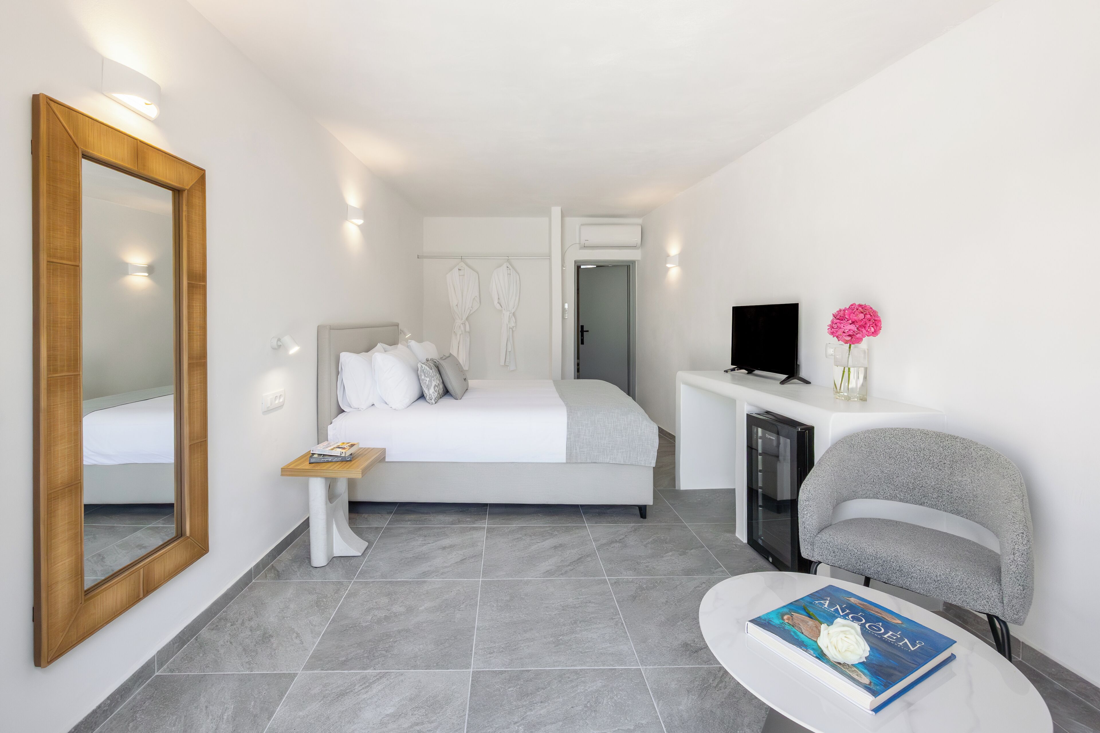 Une chambre d’hôtel moderne avec un grand lit, une table de chevet, une télévision et un coin salon avec un livre.