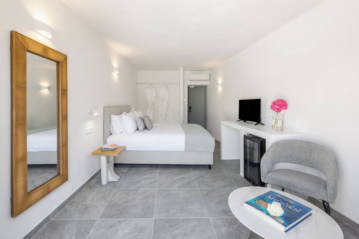 A modern bedroom with a large bed, bedside tables, a TV, and a seating area with a book.