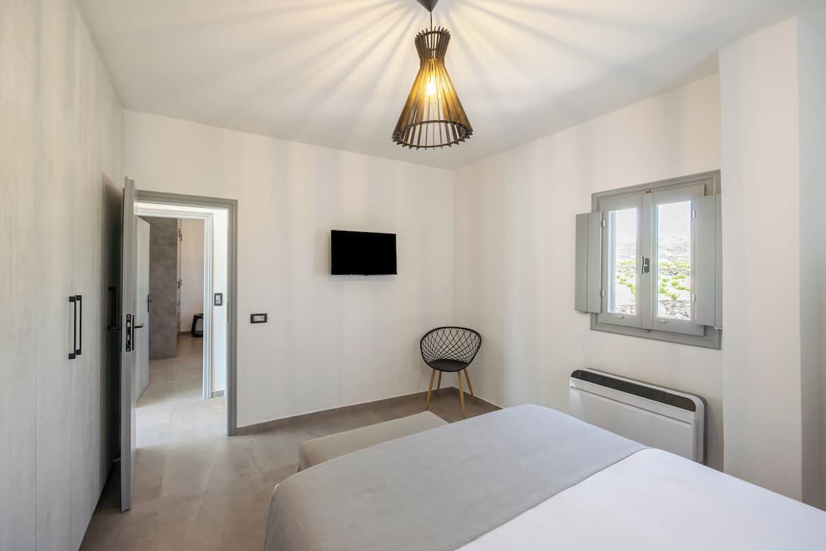 A modern bedroom with a bed, a chair, a TV, and a window.