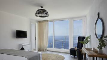 Una habitación de hotel con una cama, un escritorio, una silla, un televisor, un ventanal con vistas al mar y una lámpara de techo.