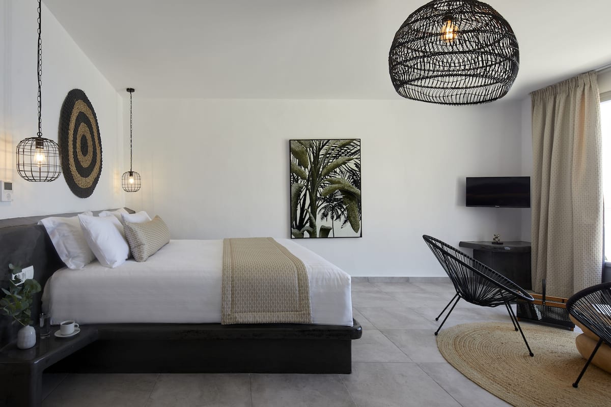 A modern bedroom with a bed, a side table, a chair, a TV, and a large woven light fixture.