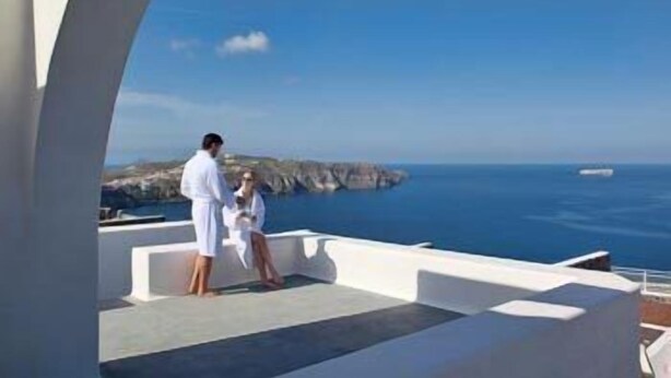 Una pareja en un balcón con vistas a la costa, acantilados y el mar.
