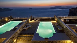 Piscina infinita en la azotea con sillones de descanso y vistas al atardecer.