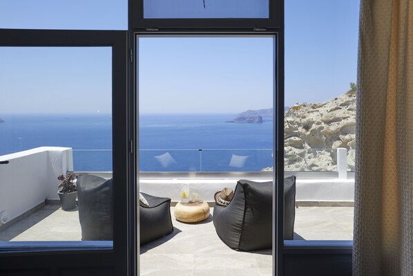 Un balcón con dos sillones negros acolchados, una mesita redonda con un florero y una planta, y vistas al mar y un paisaje rocoso.