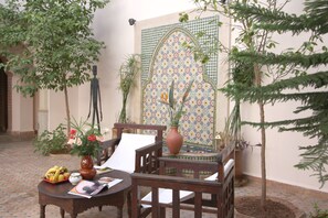 Ein traditioneller marokkanischer Innenhof mit einer mit Fliesen verzierten Wand, einem Holztisch mit Blumenvase und Topfpflanzen.