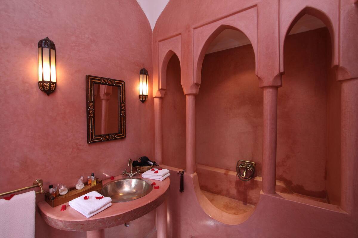 A bathroom with a pink wall, a sink with a mirror, and two wall-mounted lights.