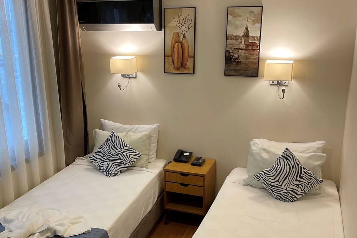 A hotel room with two beds, a nightstand with a phone, wall-mounted lamps, and artwork.