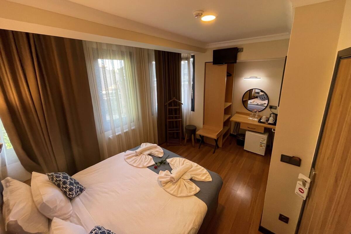 A hotel room with a bed, a desk, a chair, a mirror, and a television.