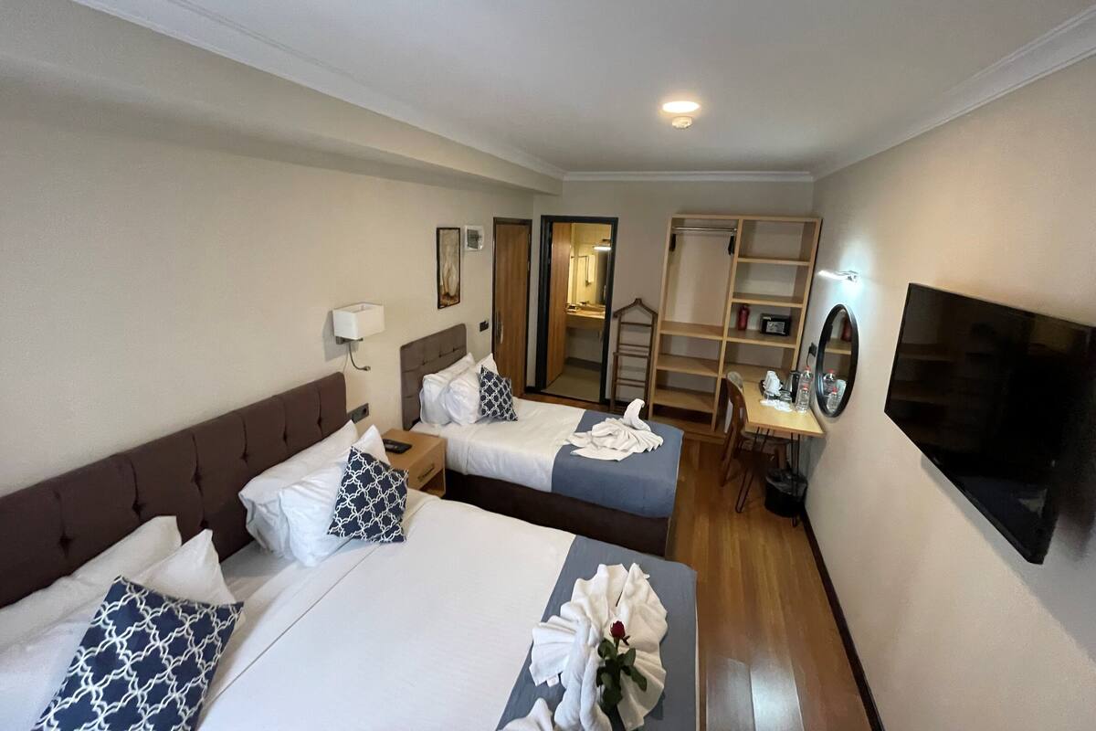 A hotel room with two beds, a TV, a desk with a chair, a wardrobe, and a bathroom visible through an open door.