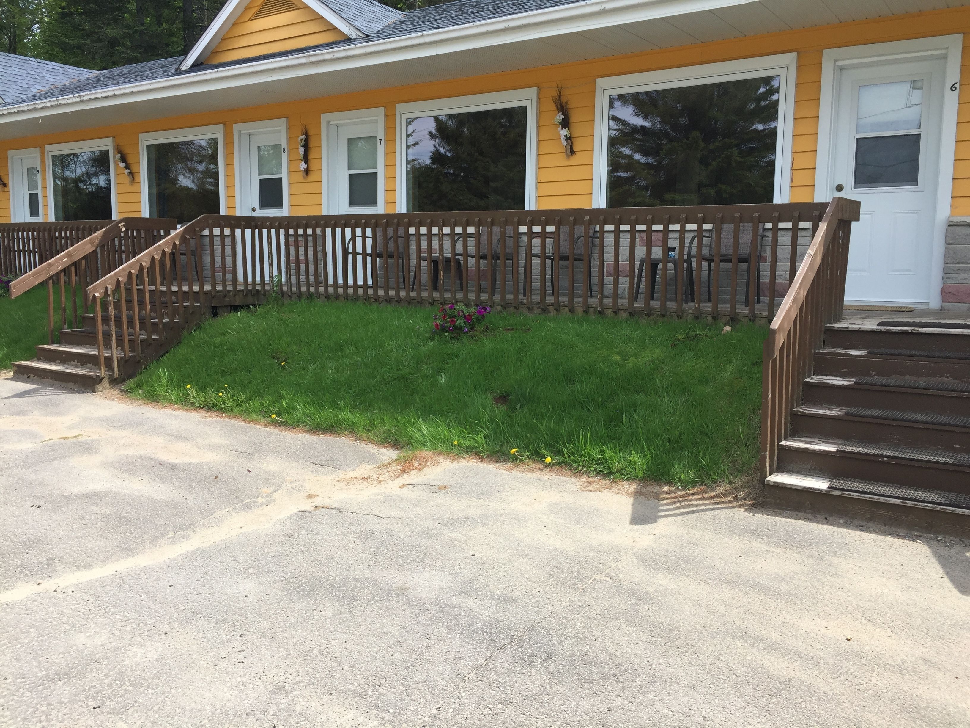A yellow building with a wooden porch and a staircase leading to the entrance.