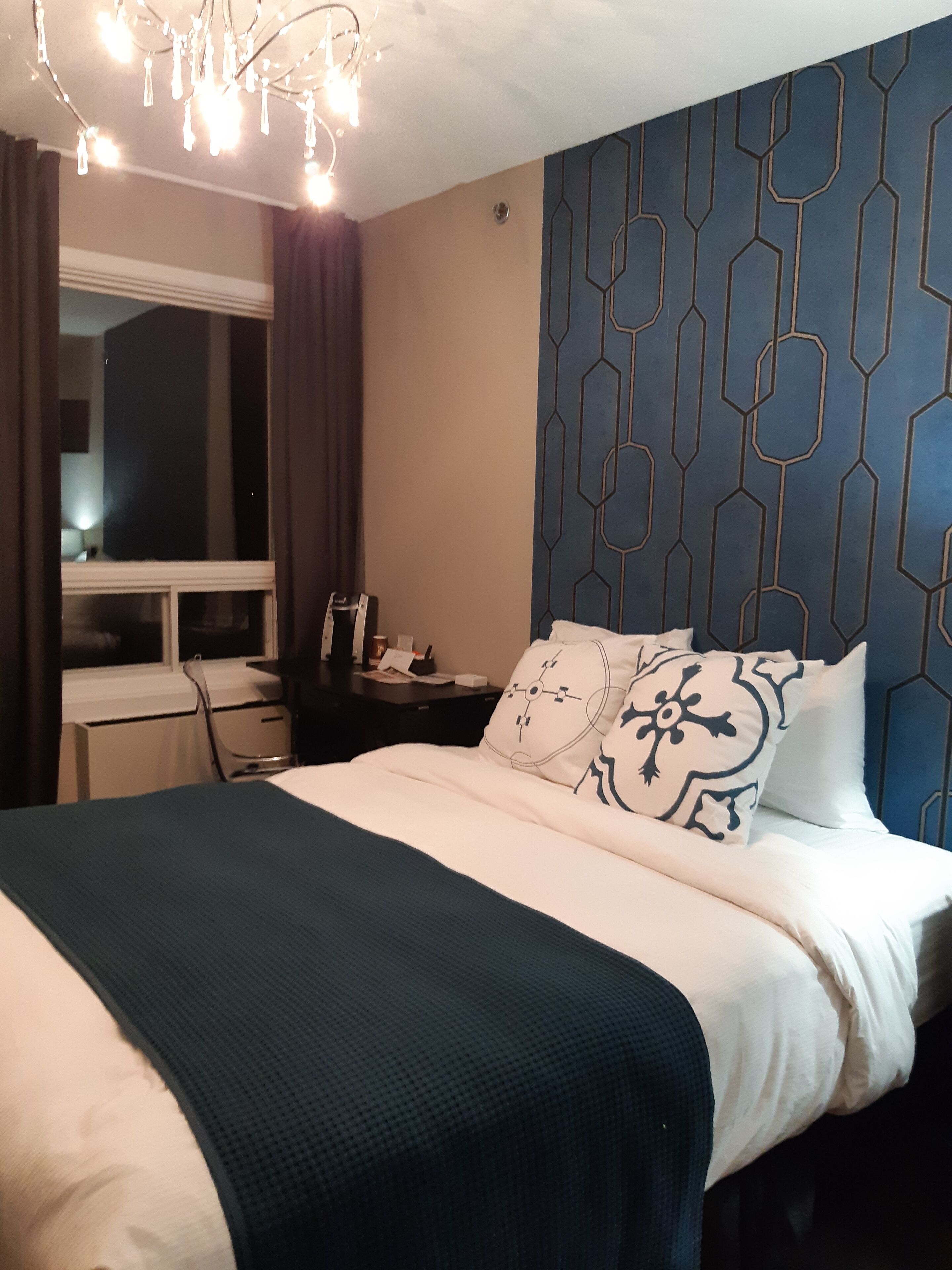 Une chambre d’hôtel avec un lit, une table de chevet, un bureau et une fenêtre avec des rideaux.