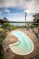 Una piscina de diseño curvo, rodeada por una cerca metálica y con vistas a una extensión de agua.