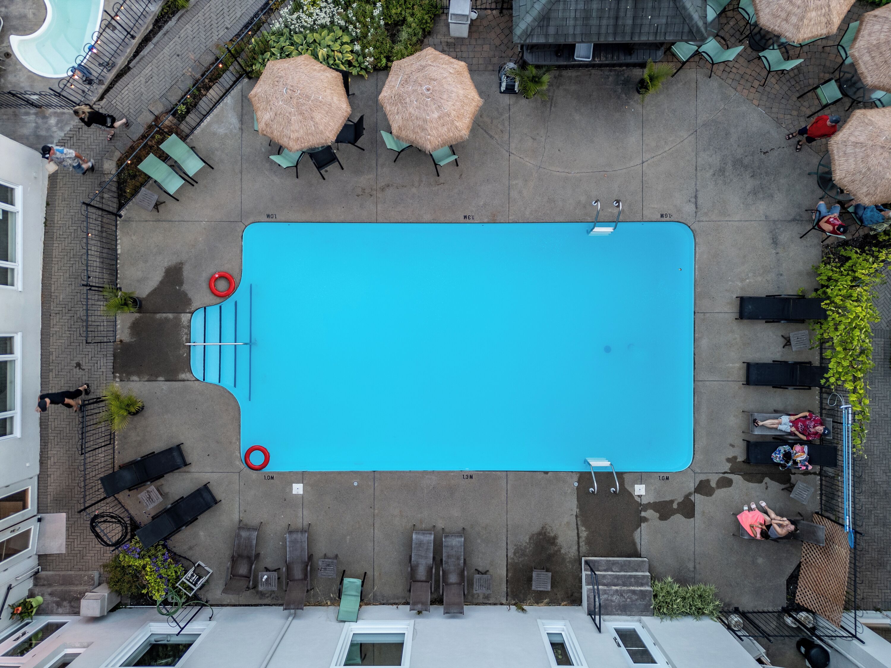 An aerial view of a swimming pool surrounded by lounge chairs, umbrellas, and potted plants.