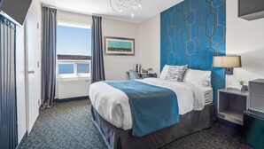 Habitación de hotel con una cama grande, vista al mar, diseño geométrico en la pared azul y un candelabro.