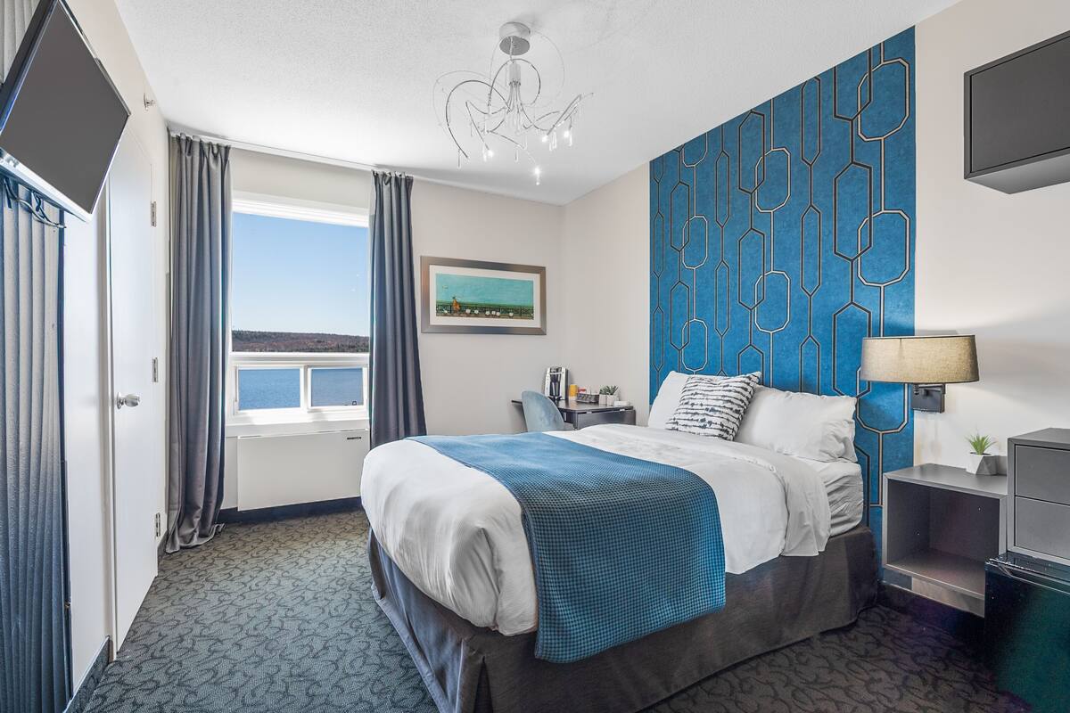 Habitación de hotel con una cama grande, vista al mar, diseño geométrico en la pared azul y un candelabro.