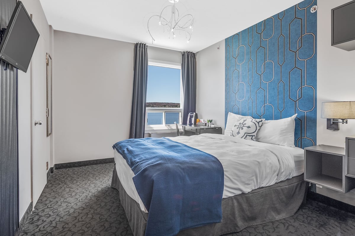 Habitación de hotel con cama, escritorio, silla, televisión y ventana con cortinas.