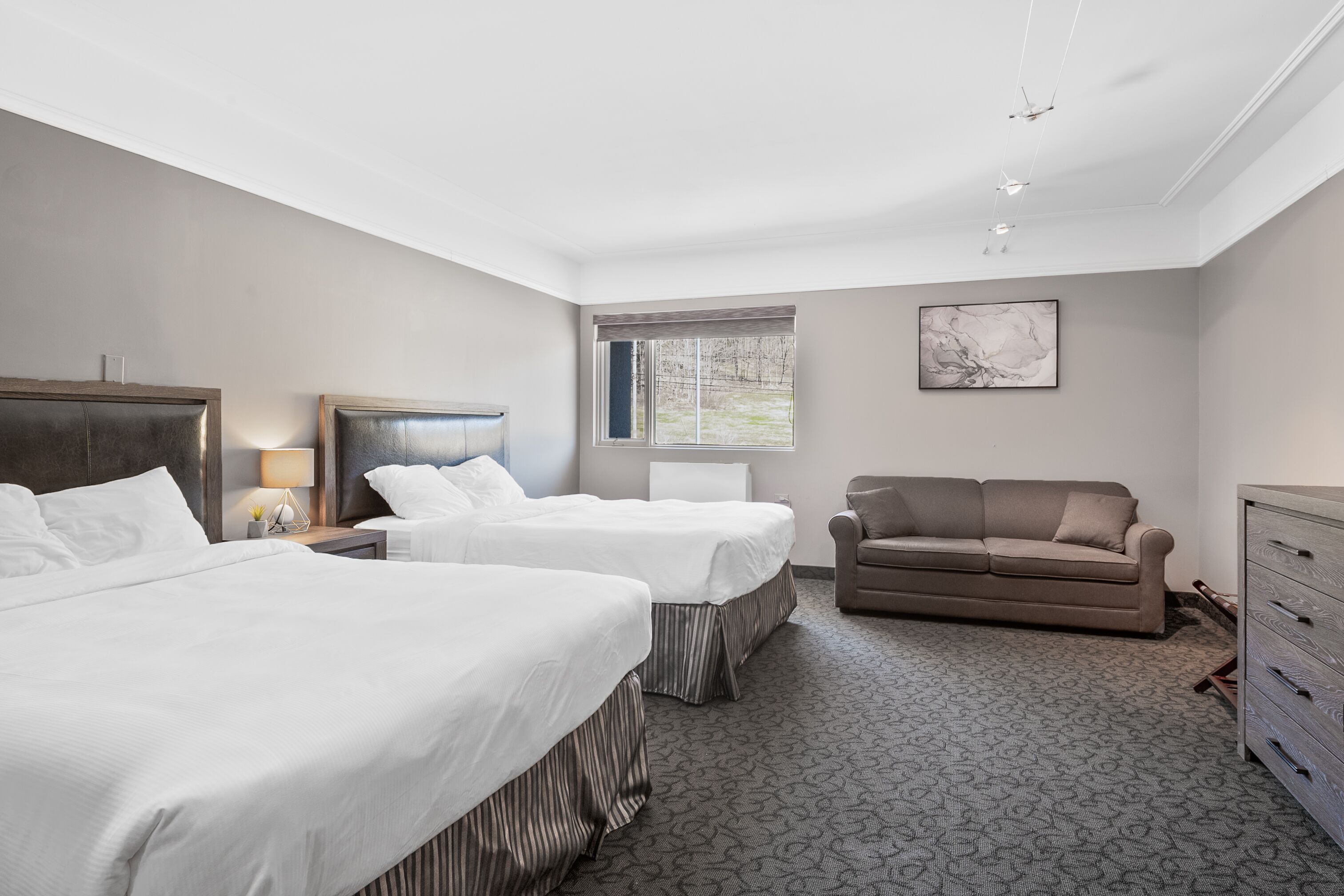 Habitación de hotel con dos camas, un sofá, un aparador y una ventana con vista a árboles.