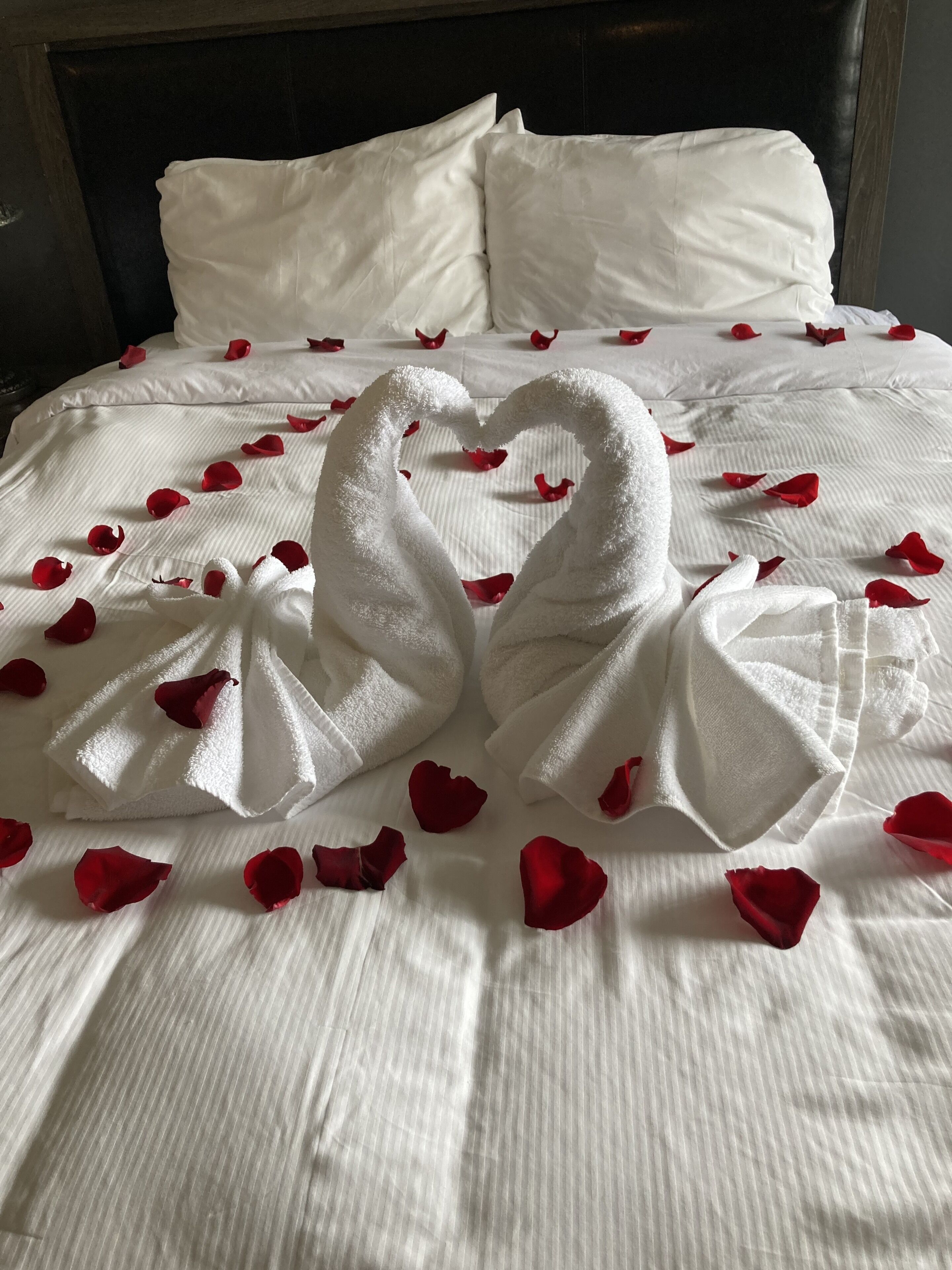 Una cama con sábanas blancas y un arreglo de toallas en forma de corazón.